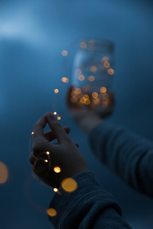 Hands holding a string of lights with a short depth of field focused on one tiny bulb
